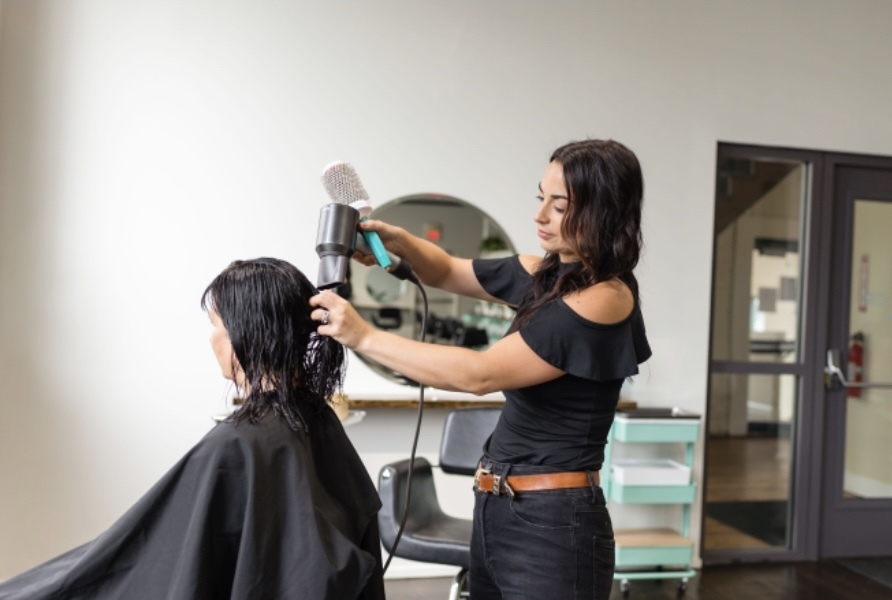 A hairstylist is blow-drying a client's wet hair in a modern salon.